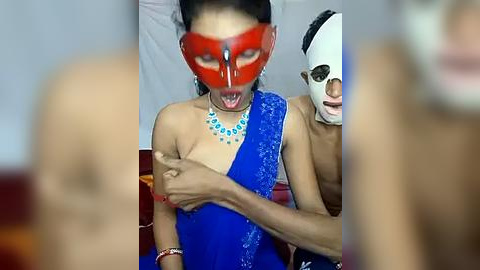 Media: Video of a woman in a blue sari, wearing a red mask, with a man's hand touching her breast, surrounded by two other masked people.