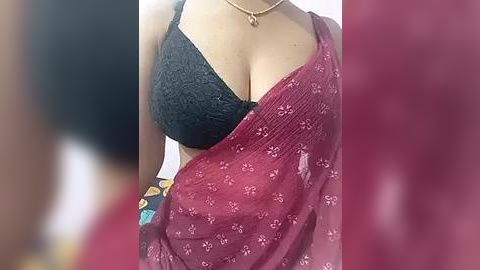 Media: Video of a woman's upper body, showcasing a black lace bra and a maroon sari with floral patterns. Her fair skin and a gold necklace are visible.