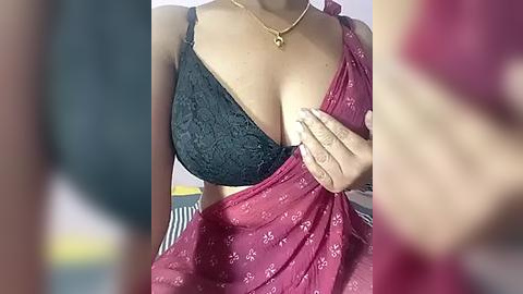 Media: A video of a woman with light brown skin, wearing a black lace bra and a pink sari with floral patterns. Her left hand covers her right breast, partially visible.