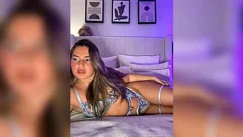 Media: A blurry video of a woman in a floral bra and panties lying on a bed, surrounded by minimalist art and purple lighting.