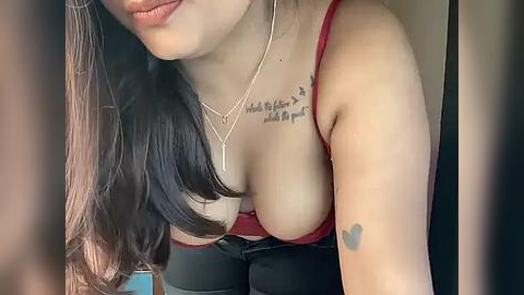 Media: A close-up video of a light-skinned woman with long, dark hair, wearing a red bra, revealing cleavage, and a black heart tattoo on her arm.