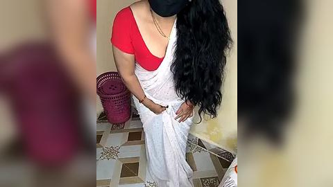 Media: Video of a South Asian woman in a white saree with red blouse, black mask, holding a bucket, standing on a tiled floor.