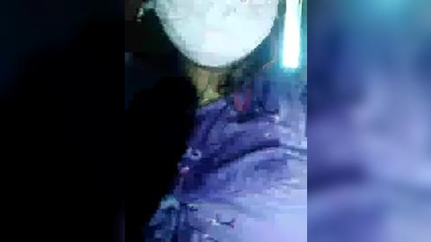 Media: A grainy, low-resolution video shows a dark, shadowy figure in a dimly lit, blue-hued room. The figure's identity and details are obscured. The background has indistinct shapes and textures, suggesting a surreal or mysterious atmosphere.