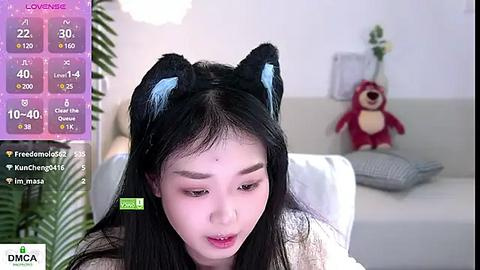 Media: A video shows a young East Asian woman with black hair, wearing cat ears, sitting on a couch. The background includes a white wall, a stuffed bear, and a potted plant. A live stream screen shows stats and viewers.