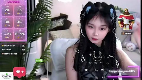 Media: Video of an East Asian woman with long black hair in braids, wearing a black dress with white floral patterns, seated in a modern living room with plants and white furniture.