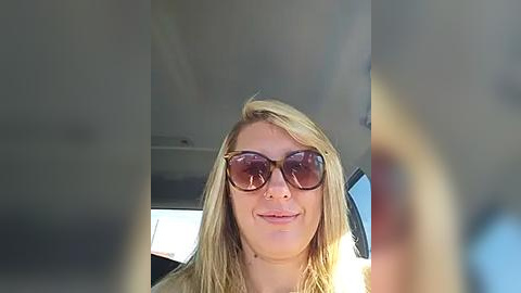 Media: A video of a smiling woman with blonde hair, wearing sunglasses, sitting in a car with the sun shining through the window.