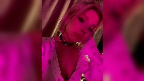 Media: Video of a blonde woman in a low-cut, white floral dress with a black choker, bathed in pink neon light, blurred background.