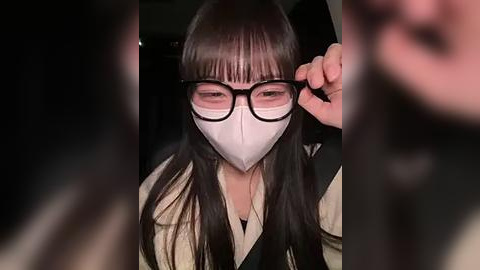 Media: Video of an Asian woman with long black hair and bangs, wearing black-framed glasses and a white face mask, adjusting her glasses in a dimly lit room.