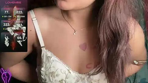 Media: A video of a young woman with long brown hair, wearing a white lace bra, showing a heart-shaped bruise on her shoulder. Background includes a smartphone screen with health and temperature data.