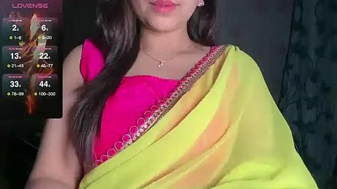 Media: Video of a woman in a bright pink blouse and yellow saree, with a background showing a live streaming screen displaying \"Lovense\" and a flower.