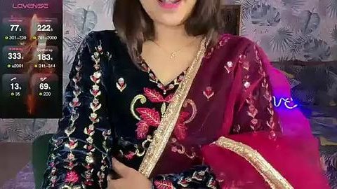 Media: Video of a South Asian woman wearing a black and red floral embroidered saree, smiling with medium skin tone, in a dimly lit room with a digital livestream overlay showing chat reactions.