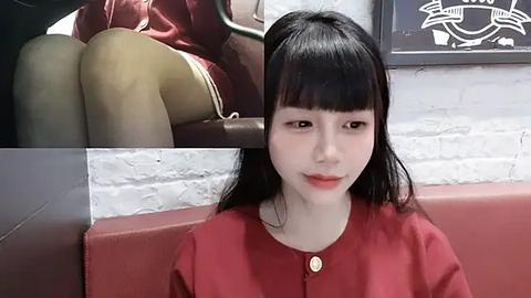 Media: Video of a young East Asian woman with long black hair and fair skin, wearing a red top, seated in a red leather booth. Background shows a white brick wall and a partially visible sign.