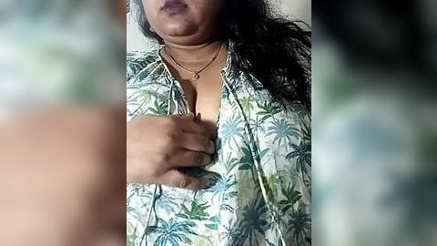 Media: Video of a South Asian woman with medium-brown skin, wearing a floral-patterned blouse, revealing her cleavage, with dark hair and dark lipstick, holding her left breast.