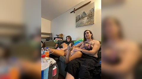 Media: Video of three women on a couch in a living room; one breastfeeding, one holding a baby, and the third watching TV. Background includes a painting, fan, and cluttered coffee table.