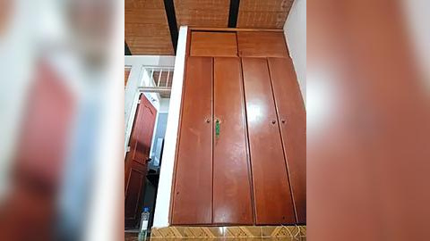 Media: Video of a spacious, rustic bathroom featuring a wooden wardrobe with multiple drawers and a green handle, set against a beige tiled floor. The room has a ceiling with exposed wooden beams and a window partially visible on the left.