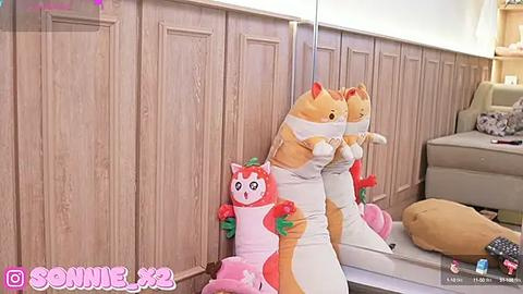 Media: Video of a plush toy cat with a white and orange fur pattern, wearing a mask, sitting on a beige sofa in a modern living room with wooden paneling.