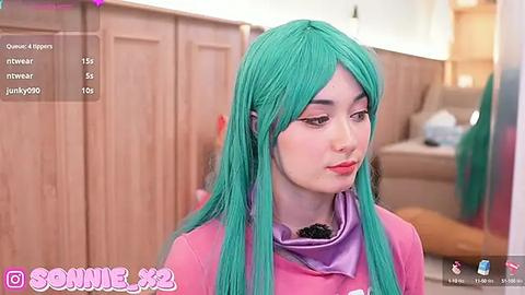 Media: Video of a young Asian woman with long turquoise hair, wearing a pink top, in a modern, light-toned room. Social media app interface visible in the bottom left corner.