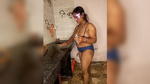 Media: A video of a dark-skinned woman with medium build, wearing a blue bikini and a red headband, standing in a cluttered, tiled bathroom with a sink and mirror.