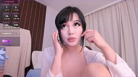 Media: A video of a young East Asian woman with short black hair, wearing a white shirt, adjusting her earpiece in a modern, minimalistic bedroom setting.