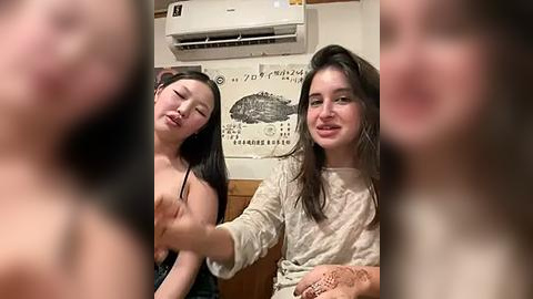 Media: Video of two young women, one topless, in a cozy indoor setting with Japanese decor, including a fish poster and air conditioner.