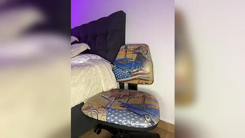 Media: A video of a modern black office chair with a colorful, patterned seat depicting a vintage car, parked against a white wall. The chair sits on a light wood floor, and the scene is softly lit with purple ambient lighting.