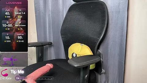 Media: Video of a black office chair with a yellow hard hat, positioned against a gray curtain. A smartphone displaying a video call is visible on the left, with a pink dildo on the desk.