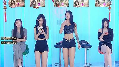 Media: Video of four Asian women in casual black outfits, seated in a studio with blue backdrop and numbered photos, holding phones, appearing focused.