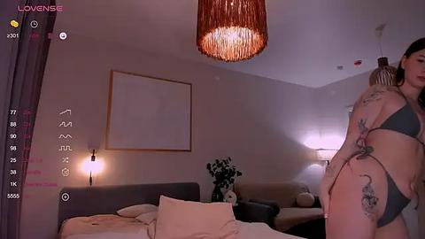 Media: A video of a dimly lit bedroom showing a couple kissing, with tattoos visible on their bodies, and a minimalist decor with a hanging light fixture.