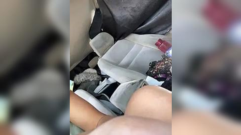 Media: Video of a car interior, showing a car seat with a partially visible infant in a white and grey car seat, surrounded by disorganized clothing and other items. The image is slightly blurred, with the focus on the car seat and child.