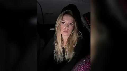 Media: A dimly lit video of a blonde woman in a black top, seated in a car, with blurry passengers in the background.