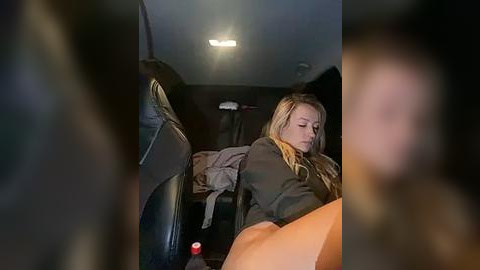 Media: A video shows a blonde woman with a serious expression, wearing a dark jacket and orange pants, sitting in the back of a dimly lit car.