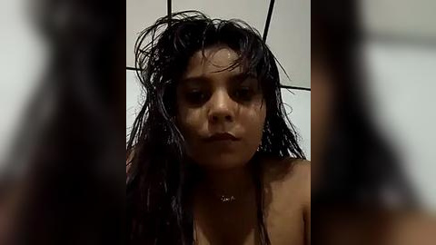 Media: Video of a young woman with long, wet black hair, wearing a strapless top, standing in a bathroom with white tiles and a black sink. The image is slightly blurred.