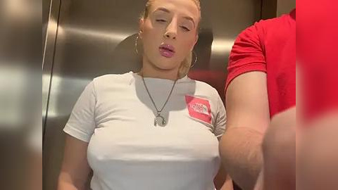 Media: Video of a curvy, blonde woman in a tight white shirt with a logo, leaning against a metal elevator door, looking sultry.