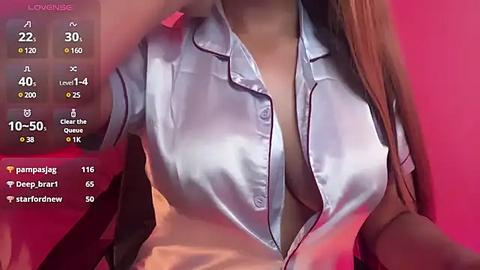 Media: A close-up video of a light-skinned woman with long, straight, light brown hair, wearing a shiny, silky, light blue blouse with a deep V-neck, partially unbuttoned, revealing cleavage.