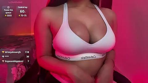 Media: Video of a woman in a white Calvin Klein sports bra, with a curvy physique and medium brown skin, in a dimly lit bedroom with pink lighting.