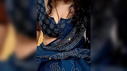 Media: Video of a woman with medium brown skin wearing a blue sari with white polka dots. She has curly dark hair, and the background is blurred, focusing on the sari's intricate details.