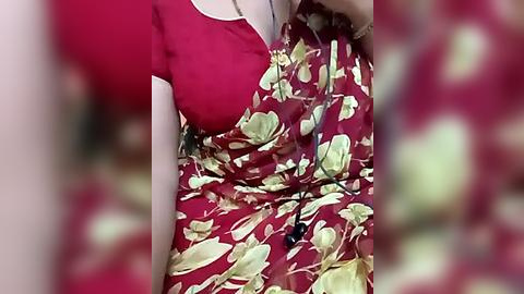 Media: Video of a woman in a red dress with a floral pattern, holding a black bag, blurred background.