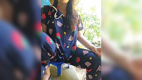 Media: A video of a person in a blue, patterned pajama set with strawberries and checkered accents, seated outdoors on a concrete surface, with blurred greenery in the background.