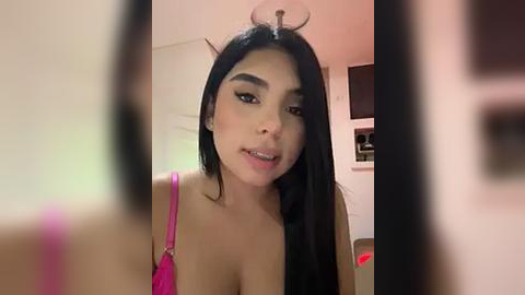 Media: A video of a young woman with long black hair, wearing a bright pink bra, captured from a selfie angle.