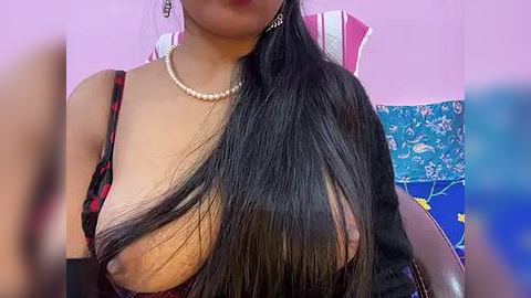 Media: Video of an Asian woman with long black hair, wearing a black and red dress with one strap down, exposing her breast, pearl necklace, in a room with blue and red decor.