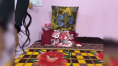 Media: A video of a cozy, colorful bedroom with a floral-patterned bedspread, a checkered floor, and decorative pillows featuring blue roses and red flowers. The walls are painted a soft pink.