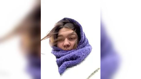 Media: Video of a young Asian woman with long black hair wrapped in a purple shawl, wearing a white sweater, against a blurred background.