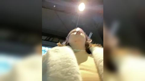 Media: Video of a person wearing a fluffy white costume with a large headpiece, standing inside a dimly lit room with a hanging light bulb. The background is blurred, suggesting a low-quality video.