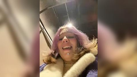 Media: Video of a woman with light skin, wearing a pink wig and fur-lined coat, with a visible metal collar around her neck, appearing distressed, indoors.