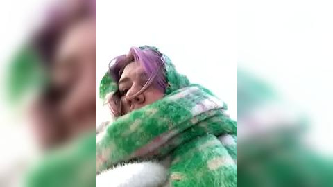 Media: A blurry video of a person, possibly a child, wearing a green and white striped blanket, with a purple headband, and resting their head on a white surface.