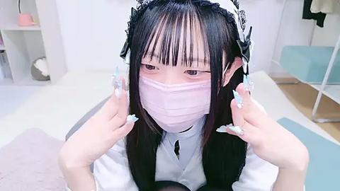 Media: Video of an Asian woman with long black hair and light skin, wearing a light pink surgical mask, white maid headband, and a white dress with a black choker. Background features a white room with shelves and a blue cushion.