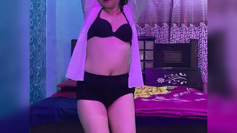 Media: Video of an Asian woman in a black bra and panties, wearing a white shirt, posing in a dimly lit bedroom with purple lighting, pink floral curtains, and a dark wooden bed.