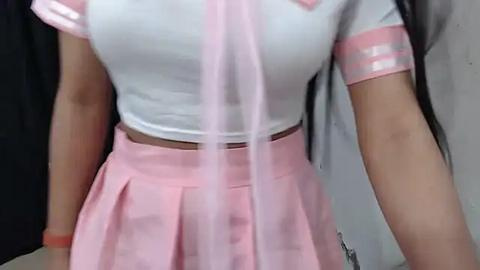 Media: Video of a woman wearing a pink sailor-style outfit with white and pink details. She has a medium build with a slim waist, and her long, dark hair cascades over her shoulders.