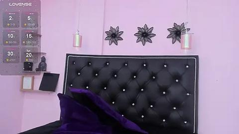 Media: Video of a modern, pink-walled bedroom with a black, tufted headboard, decorative black floral wall art, and a calendar with a purple background.