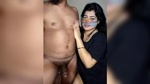 Media: A video featuring a partially nude man with a large, erect penis and a woman wearing a mask, holding a cloth over his genitals. The background is blurred.